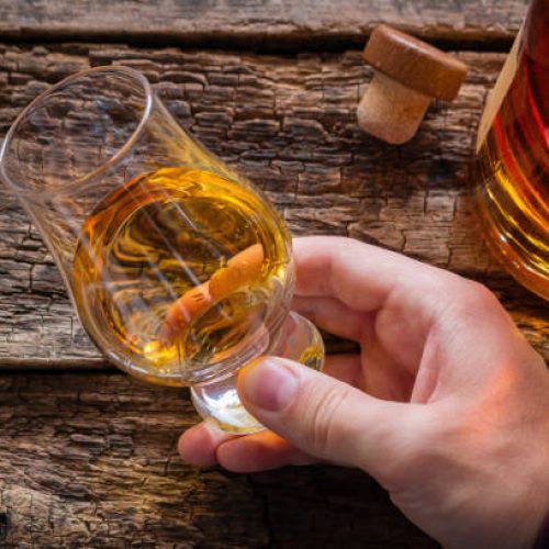 hand holds whiskey in a glass for tasting on a wooden background